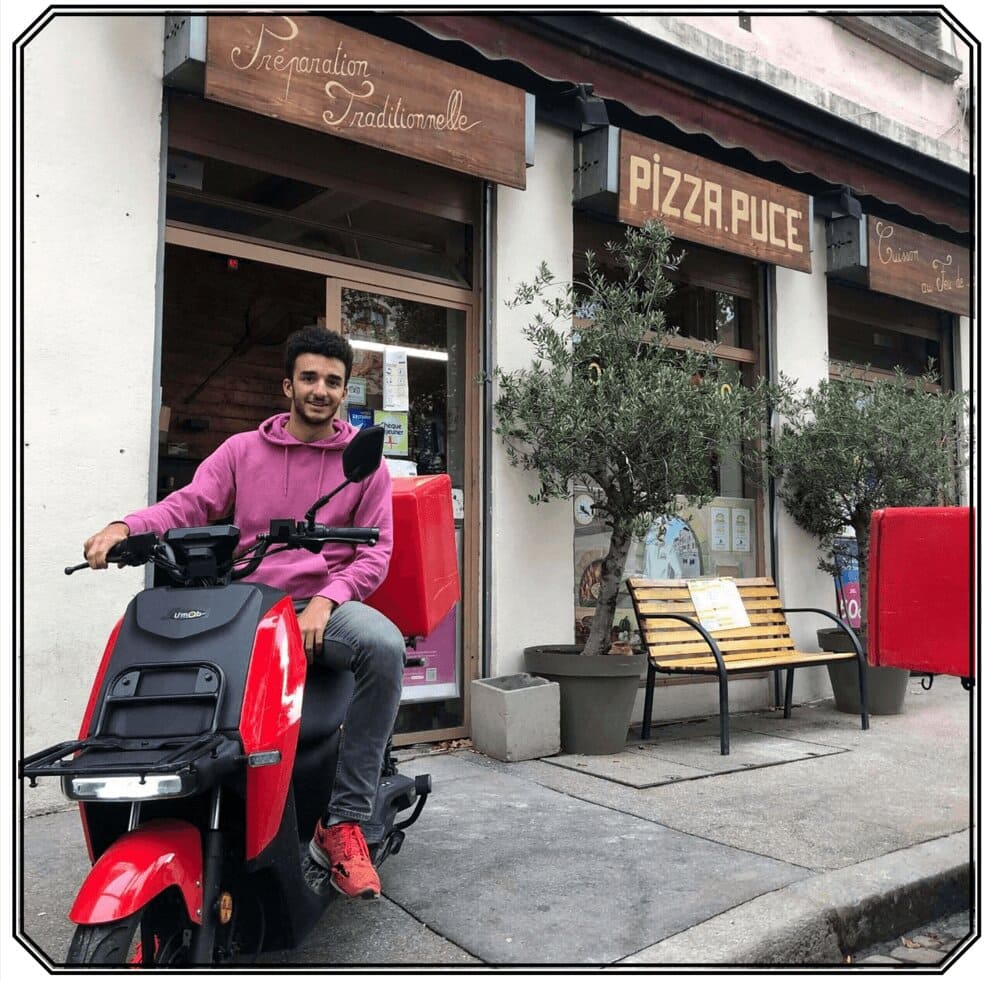 Livreur de pizza sur un scooter électrique rouge devant le restaurant Pizza Puce à Lyon
