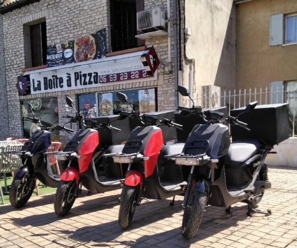 Scooters électriques garés devant le restaurant Boite à pizza