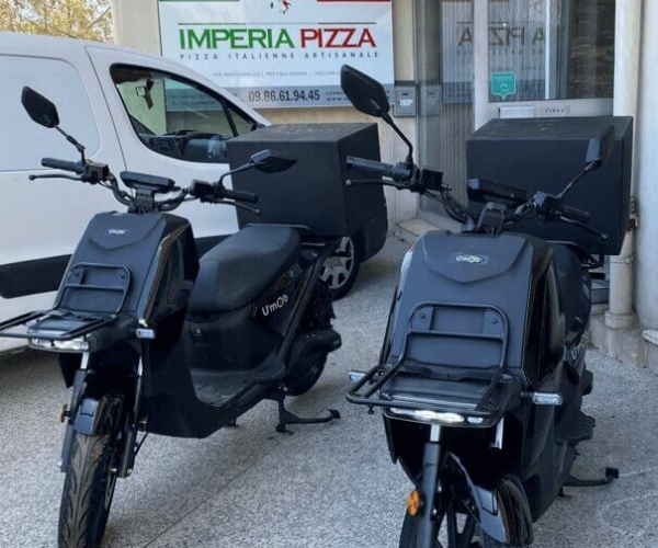 Deux scooters électriques garés devant une pizzeria