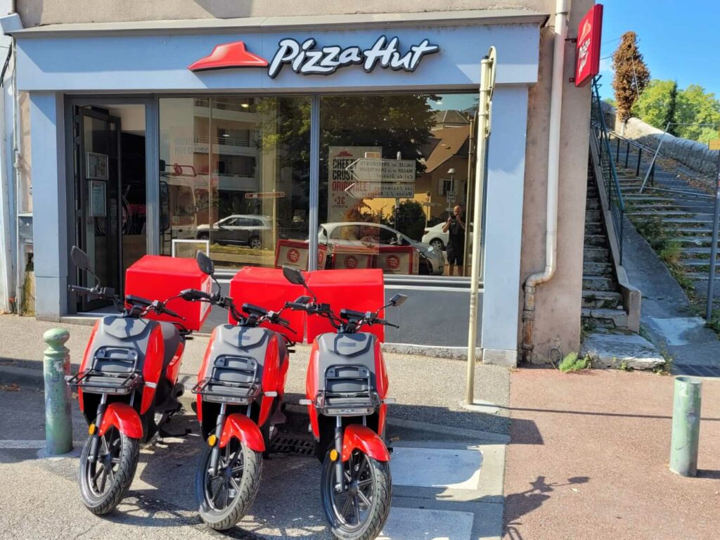 Scooters électriques rouges garés devant le restaurant Pizza HUT