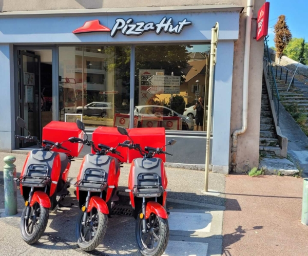 Scooters électriques rouges garés devant le restaurant Pizza HUT